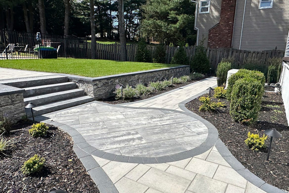 a stone walkway with a lawn and trees in the background